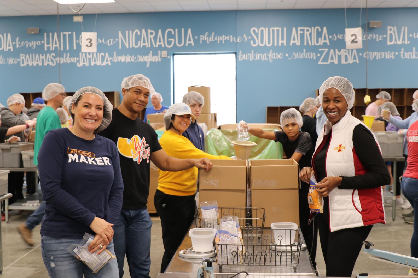 Group of 6 people wearing hairnets and smiling to camera while packaging food