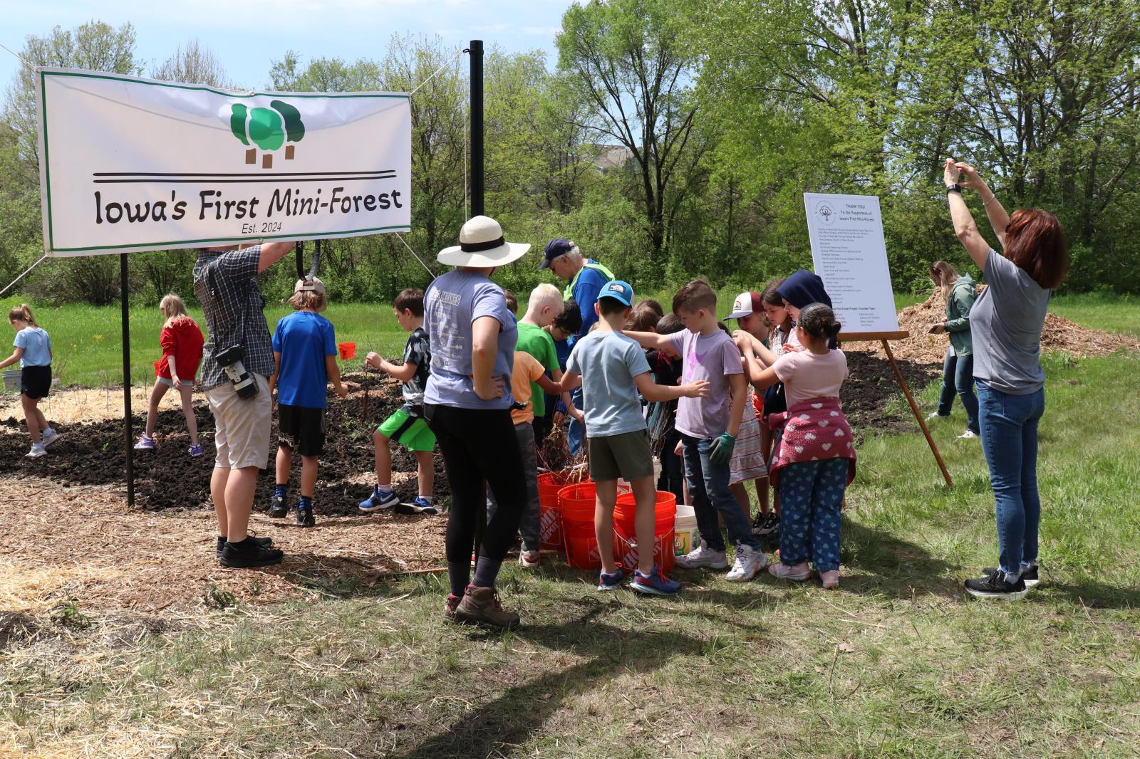 a group of adults and children get ready to plant trees in front of a banner that reads Iowa